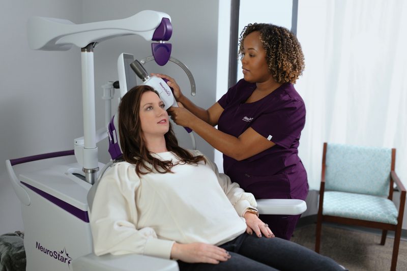 Image of patient sitting in a NeuroStar chair with physician positioning the coil on her head